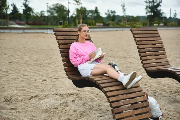 A young woman with a prosthetic leg engages in reading while wearing comfortable clothing. — Stock Photo