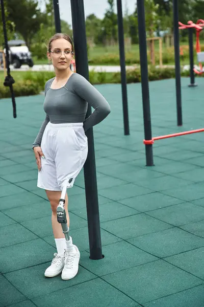 A determined young woman balances gracefully on one leg while exercising in a vibrant fitness park. — Stock Photo