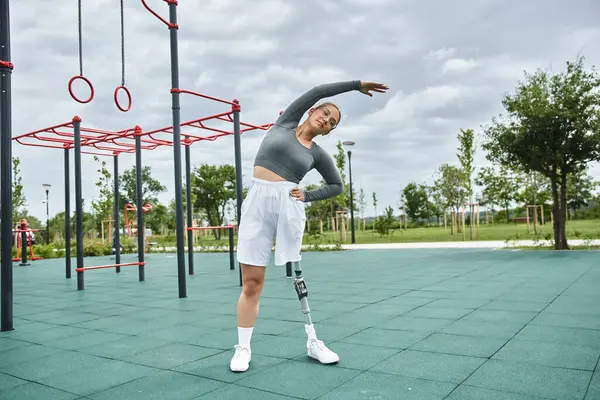 A spirited young woman with a prosthetic leg stretches outdoors in athletic gear, embracing fitness and nature. — Stock Photo