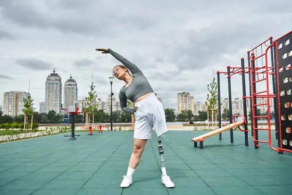 A young woman with a prosthetic leg stretches gracefully while enjoying outdoor fitness in a vibrant urban park. — Stock Photo