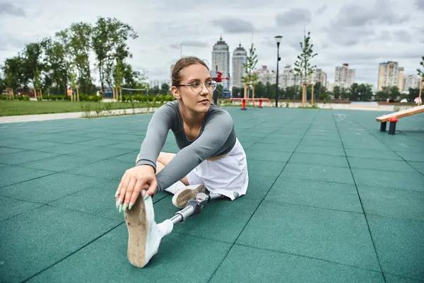 A determined young woman stretches her leg outdoors, embracing fitness and resilience in stylish sportswear. — Stock Photo