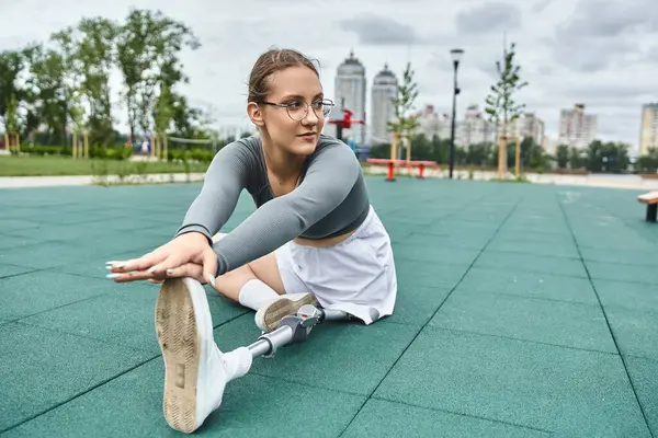 Eine entschlossene junge Frau streckt ihre Beine im Park aus und umarmt mit ihrer Beinprothese Outdoor-Fitness. — Stockfoto