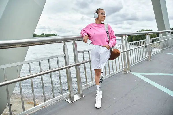 Спортивная молодая женщина слушает музыку на мосту, уверенно демонстрирует свою протезную ногу. — стоковое фото