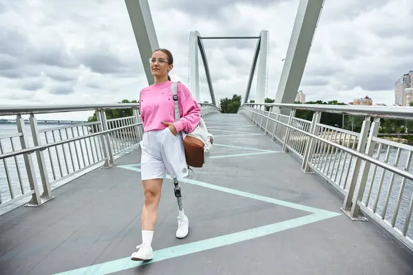A determined young woman in sportswear embraces outdoor fitness while crossing a modern bridge. — Stock Photo