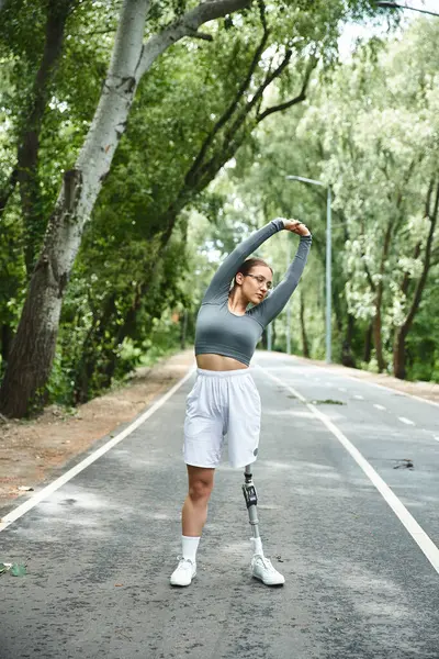 Uma jovem goza de um dia ensolarado ao ar livre, alongando-se e exercitando-se em sportswear com uma perna protética. — Fotografia de Stock