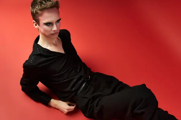 A young drag artist poses confidently in striking attire against a red backdrop. — Stock Photo