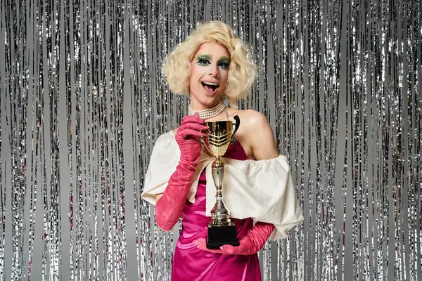 A vibrant young drag artist joyfully poses with a trophy amid shimmering decorations. — Stock Photo