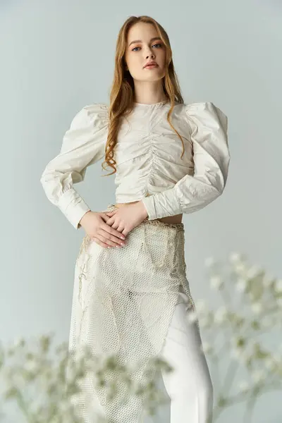 A woman elegantly poses with her hands on her hips, surrounded by delicate flowers. — Stock Photo