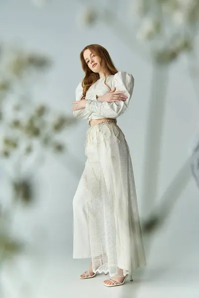 A graceful young woman stands confidently among delicate flowers. — Stock Photo