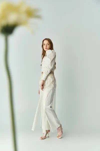 A young woman stands elegantly while surrounded by blooming flowers. — Stock Photo
