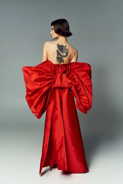A young woman showcases her bold style with a stunning red dress and captivating tattoo. — Stock Photo