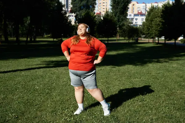 Уверенная в себе женщина plus size упражняется в наушниках в пышном зеленом парке. — стоковое фото