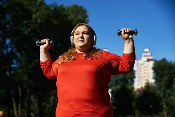 Uma mulher confiante levanta pesos em um parque vibrante sob céus azuis claros. — Stock Photo