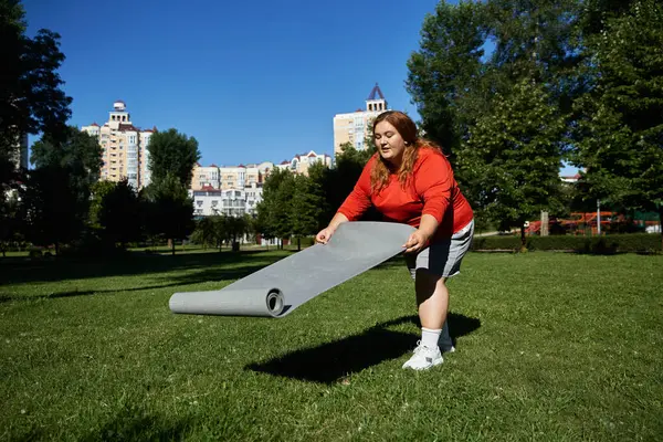 Женщина готовится к тренировкам на коврике для йоги в парке. — стоковое фото