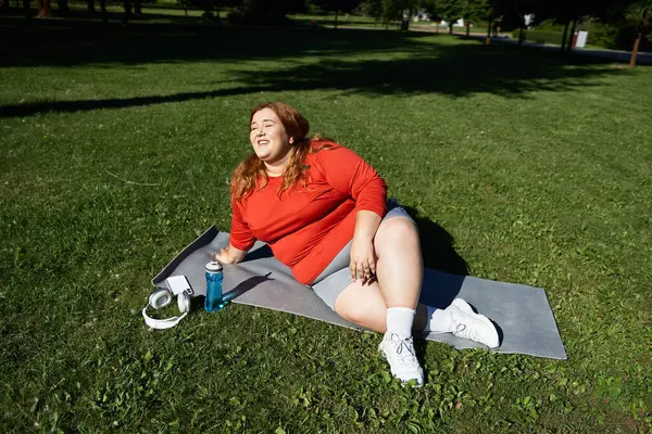 A joyful plus size woman relaxes after exercising in a sunny park. — Stock Photo