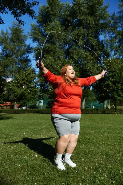 A plus size woman joyfully skips rope in a vibrant park. — Stock Photo