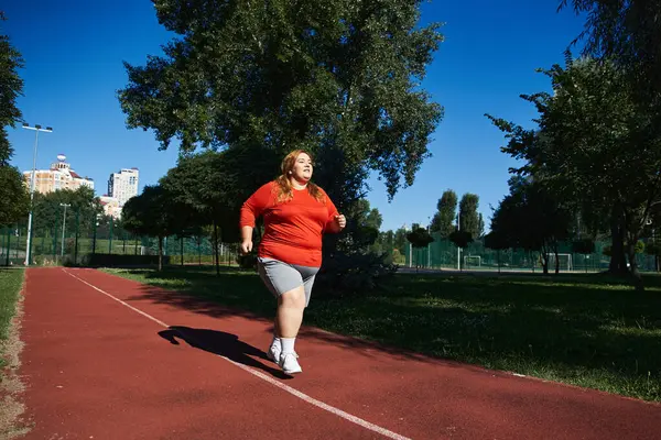 A plus size woman enjoys jogging along a vibrant park path on a sunny day. — Stock Photo