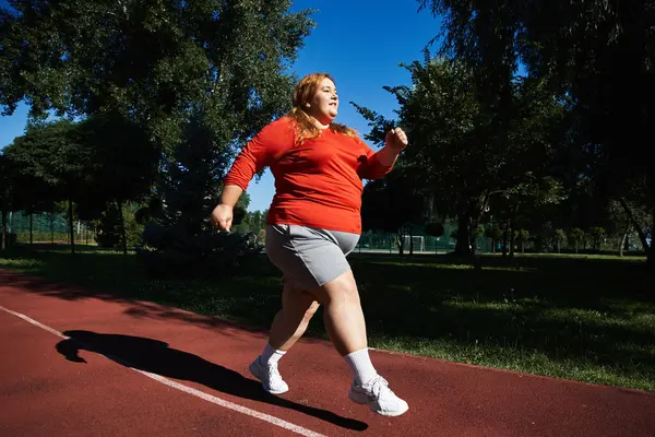 Un vibrante plus size donna jogging lungo un sentiero soleggiato parco. — Foto stock