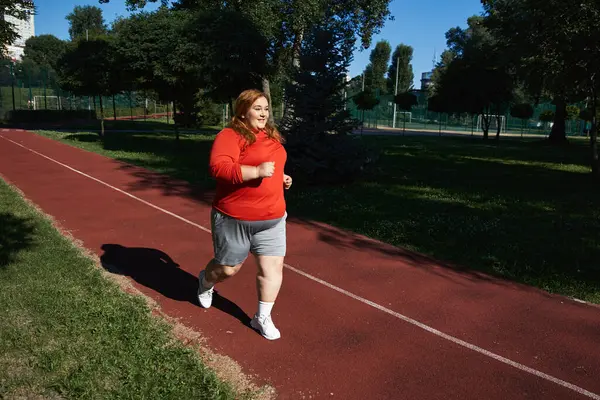 Una donna gioiosa corre su una pista, godendo il suo allenamento sotto la calda luce del sole. — Foto stock