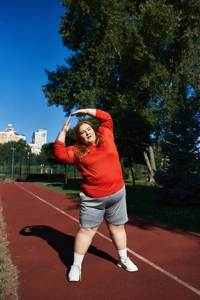 A plus size woman is stretching while exercising in a sunny park. — Stock Photo