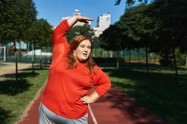 Una vibrante donna plus size gode di stretching durante il suo allenamento all'aperto. — Foto stock