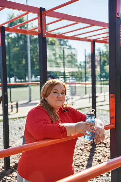 Plus size woman rests with a water bottle after working out in the park. — Stock Photo