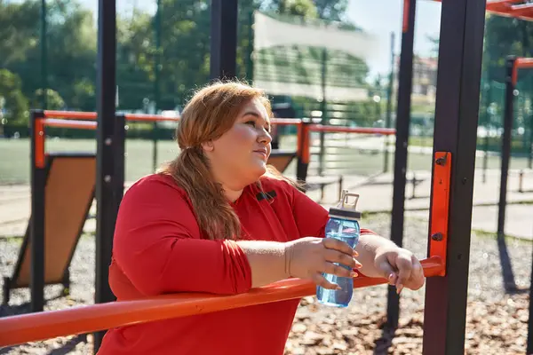 A woman pauses to hydrate during her workout in a vibrant park setting. — Stock Photo