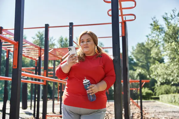 Uma bela mulher plus size se exercita ao ar livre, olhando para o telefone para orientação. — Fotografia de Stock