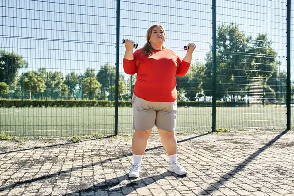 A plus size woman exercises with dumbbells in a lively park. — Stock Photo