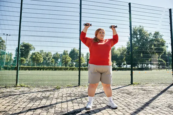 Strong woman lifts weights while enjoying a sunny park workout. — Stock Photo