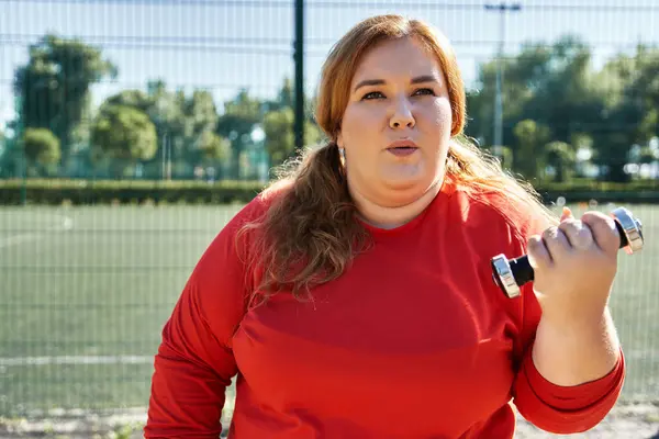 Plus size woman lifts weights while exercising outdoors in a vibrant park. — Stock Photo
