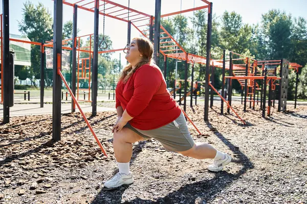 Uma mulher animada plus size se estende em um parque cercado por equipamentos de fitness. — Fotografia de Stock