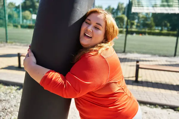 Una donna gioiosa abbraccia un palo da fitness mentre si allena nel parco. — Foto stock