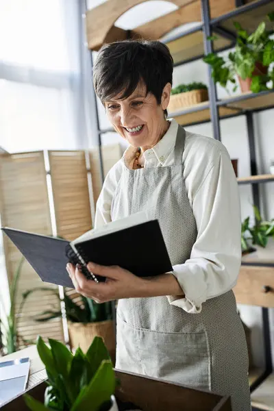 A joyful gardener reviews her notes in a cozy, plant adorned workspace. — Stock Photo