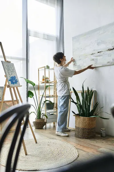 A mature woman curates her art in a sunlit studio filled with plants. — Stock Photo