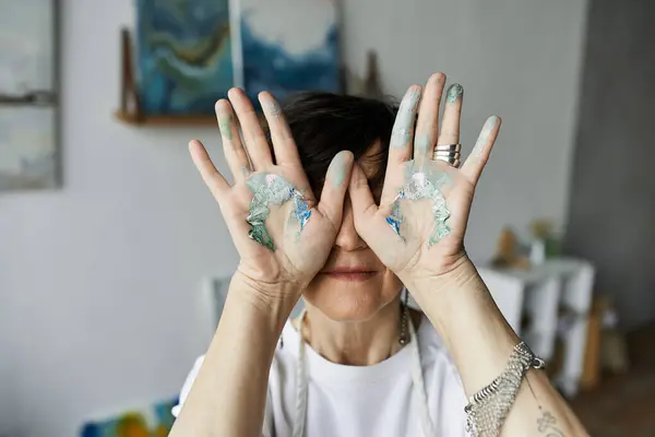 A woman playfully displays her paint stained hands while enjoying her artistic process. — Stock Photo