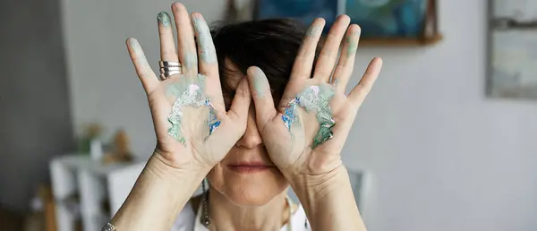 A painter joyfully shows her colorful hands while immersed in her artistic space. — Stock Photo