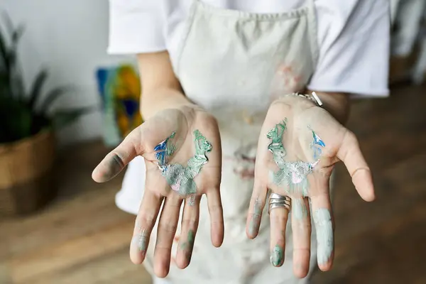 A mature artist with paint splattered hands blends colors happily in her studio. — Stock Photo