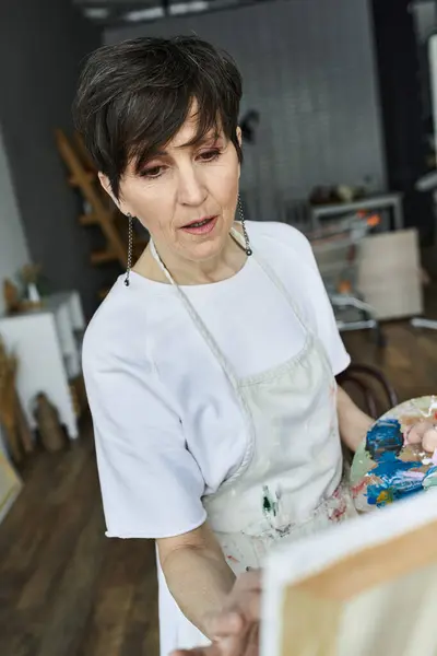 A mature woman focuses on her artwork as colors blend on her palette. — Stock Photo