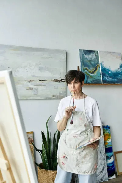 An artist reflects while holding a brush in her creative workspace. — Stock Photo