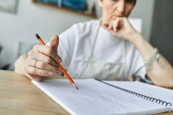 A mature woman concentrates as she sketches in her cozy art studio. — Stock Photo