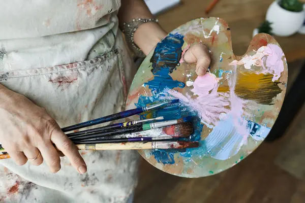 A dedicated painter mixes colors while surrounded by her artistic tools. — Stock Photo