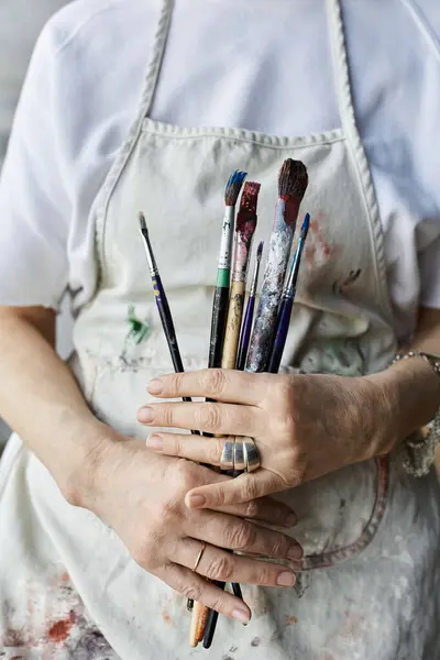 A woman in an art studio holds her paintbrushes while immersed in creativity. — Stock Photo