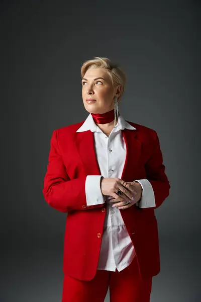 Una mujer adulta elegante con un llamativo traje rojo emana confianza en un entorno minimalista. - foto de stock