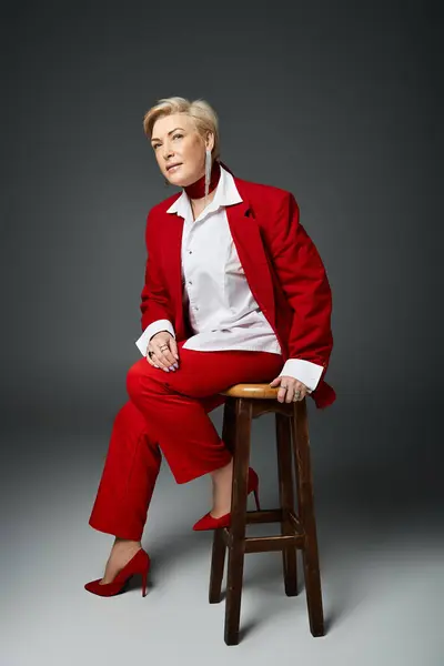 A stylish woman in a chic red outfit sits confidently on a wooden stool. — Stock Photo