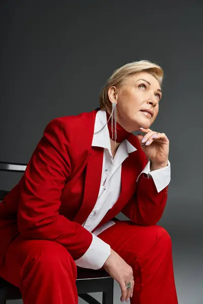 A stylish woman in a vivid red suit sits elegantly, lost in thought against a neutral background. — Stock Photo
