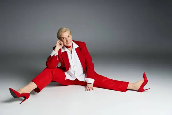 An adult woman showcases her elegance in a vibrant red suit, striking a confident pose. — Stock Photo