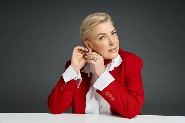 A stylish woman adjusts her ear accessories while dressed elegantly in a vibrant setting. — Stock Photo