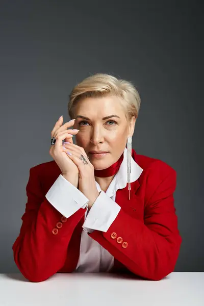 Una donna elegante vestita di rosso poggia elegantemente le mani su un tavolo, trasudando fiducia. — Stock Photo