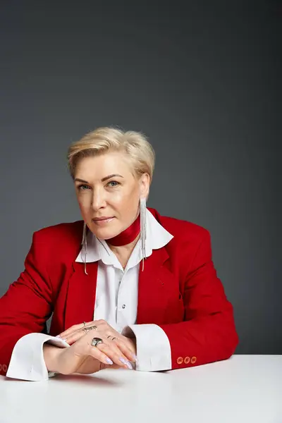 A confident woman in red stands at a sleek desk with a minimal backdrop. — Stock Photo